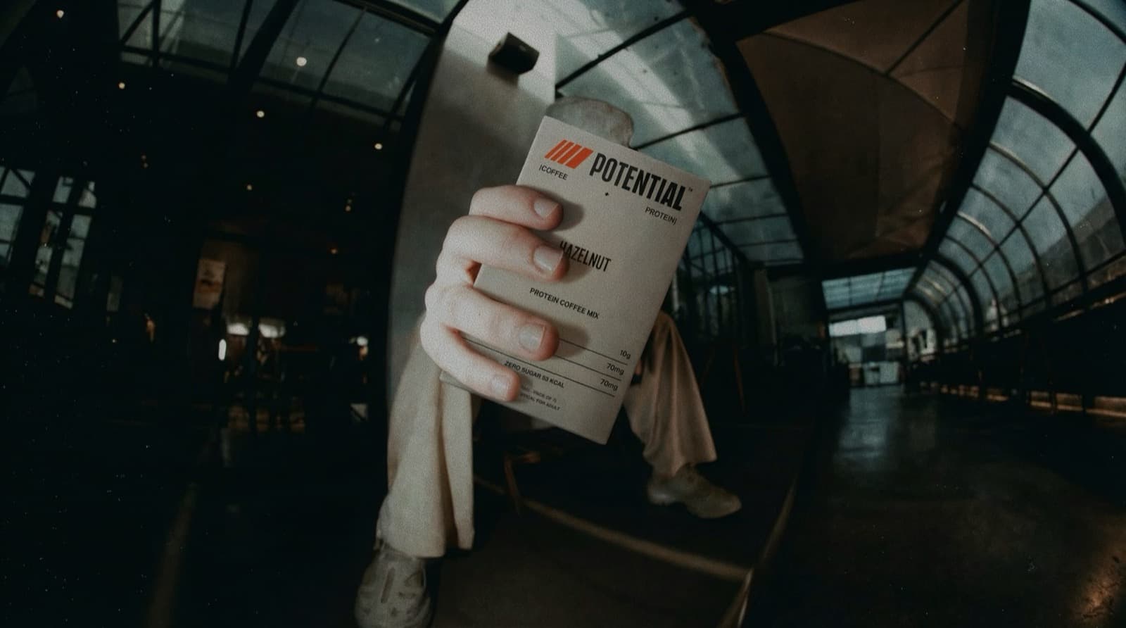 Potential — hand holding an iced latte in a branded cup, product box in frame